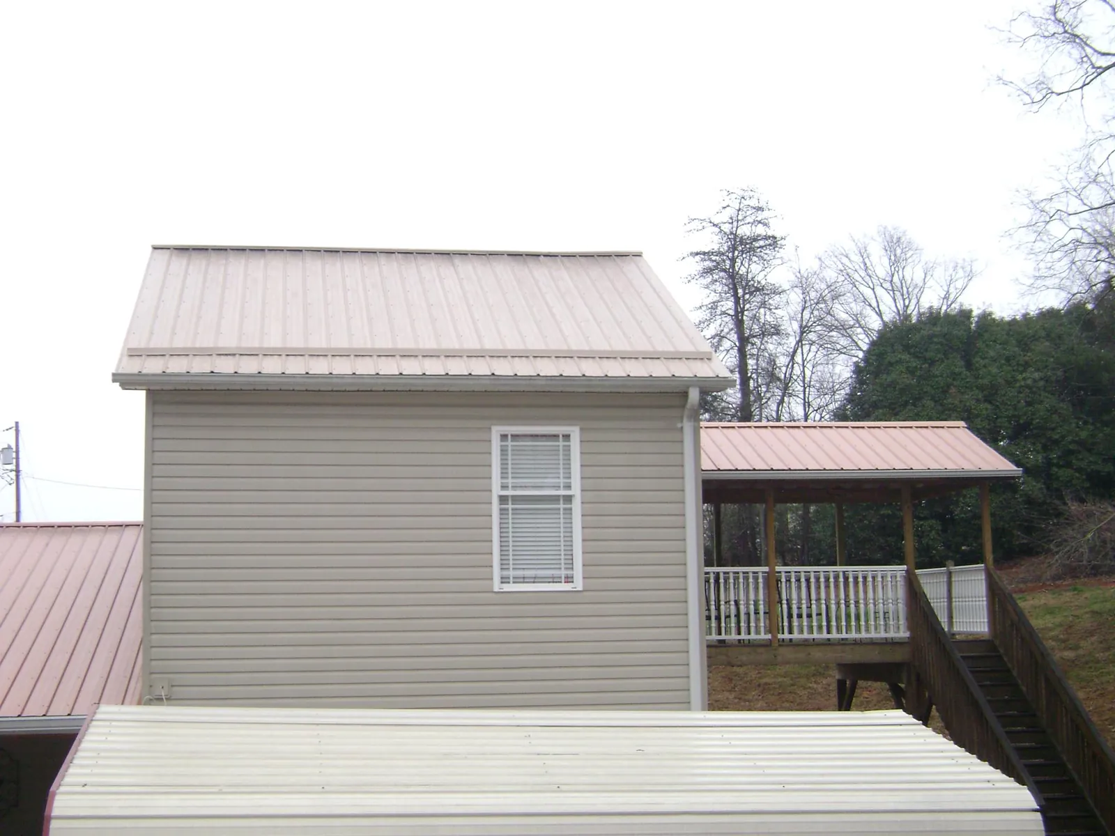 Tan metal roofs on a two story addition and attached porch, from a Roof Replacement job in Milford